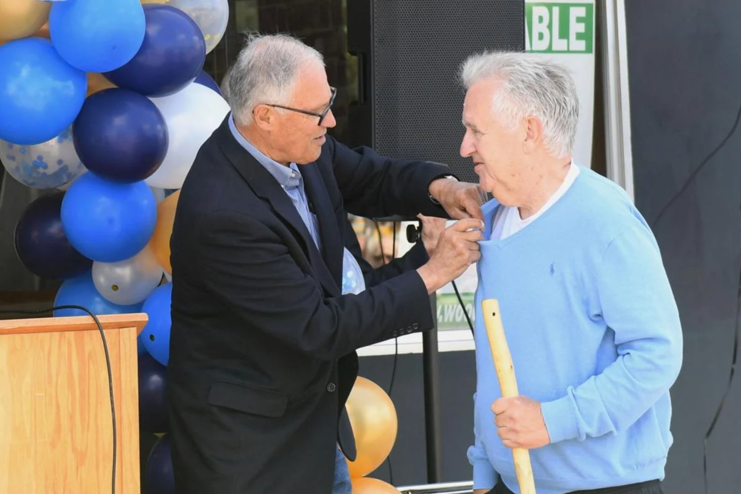 Washington Gov. Jay Inslee attaches an apple pin to Bill Ammons' shirt to honor him as "Washingtonian of the Day" at Bert and Bill Ammons' plaque dedication on Thursday, June 23 outside the family's old Pacific Barber Shop in Kelso. Inslee gave a speech at the ceremony honoring the father and son following an interview with The Daily News about the possibility of a state gas tax pause.